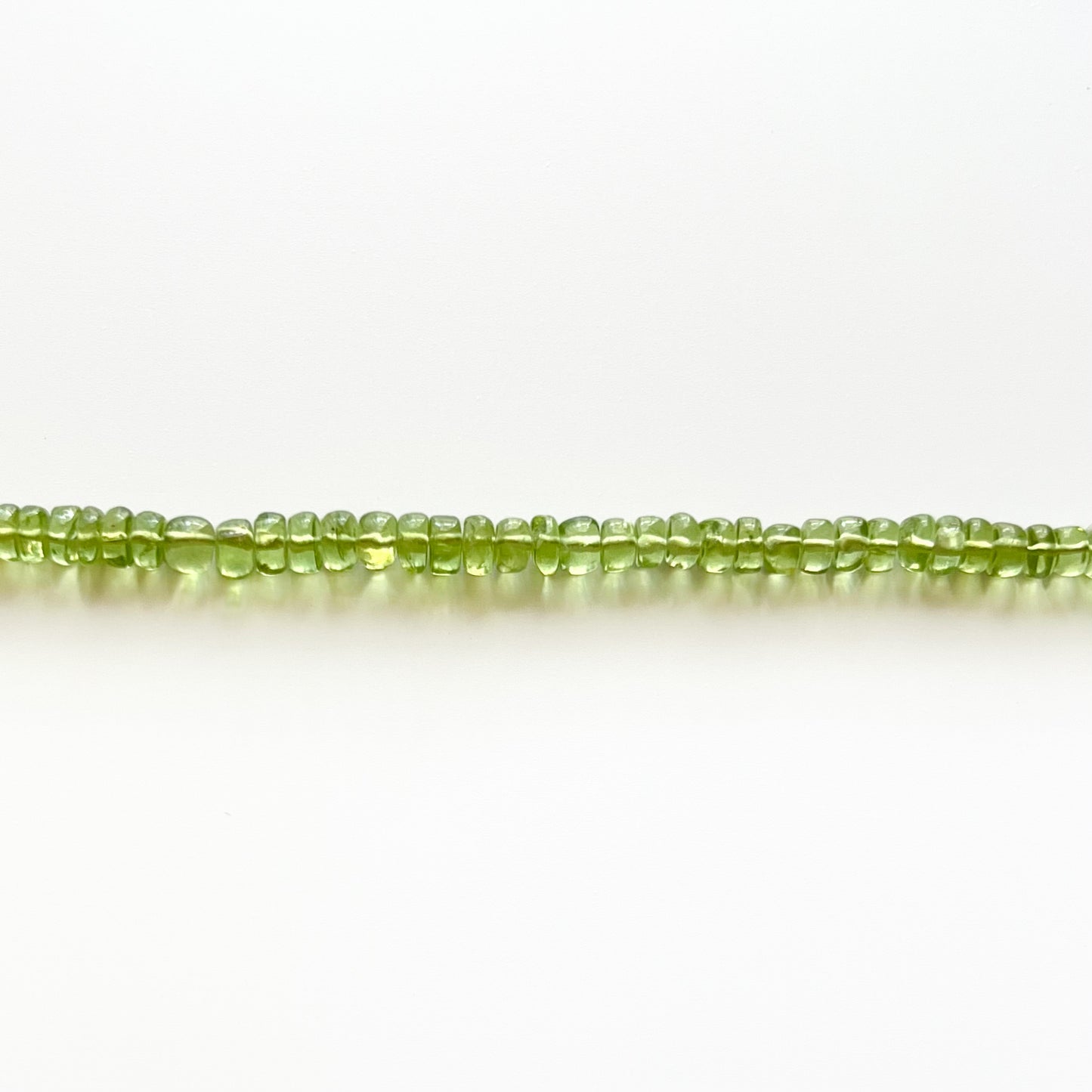 Close up of strand of green peridot beaded gemstone necklace with smooth rondelle beads
