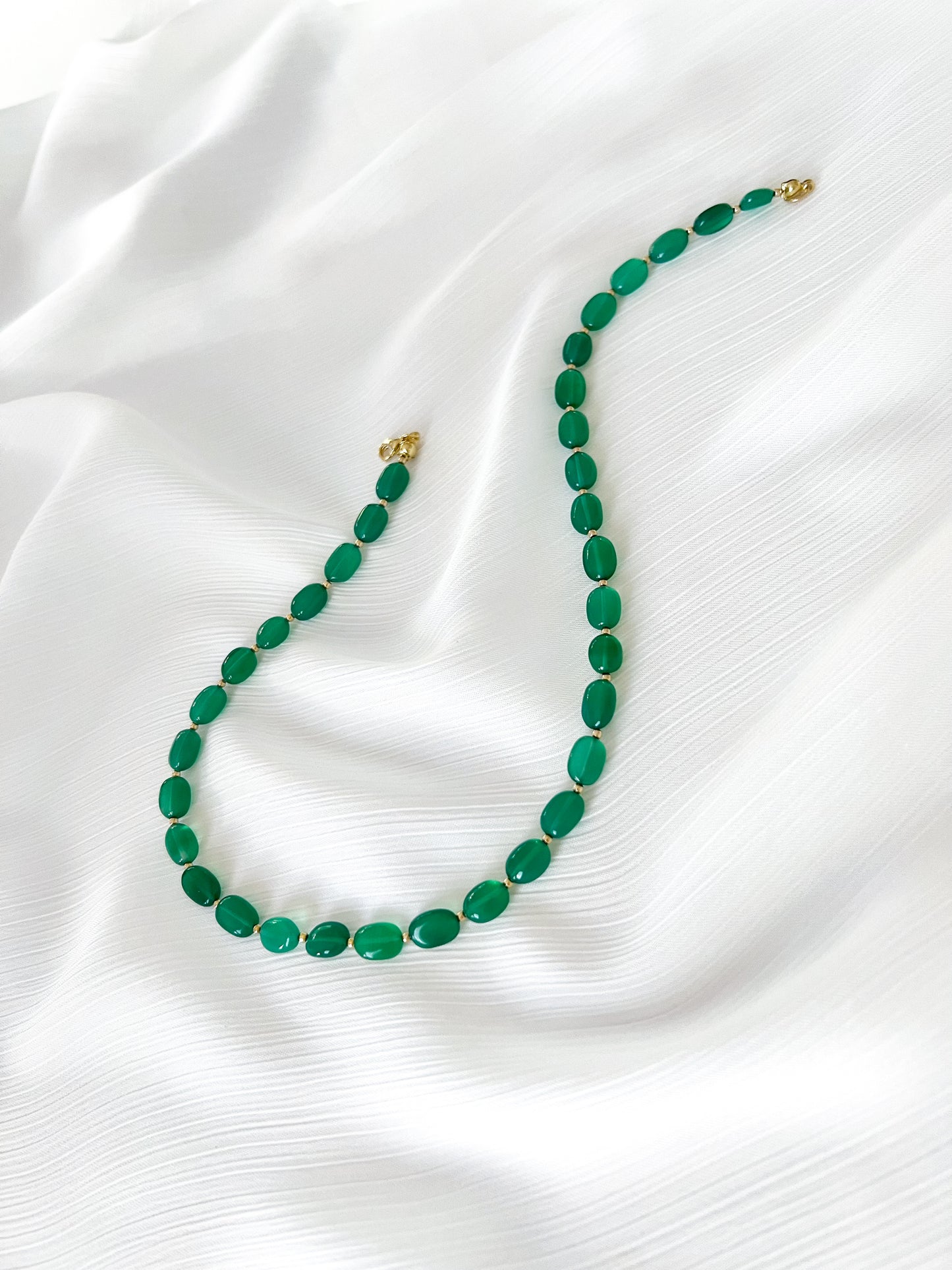 Green onyx beaded gemstone necklace with smooth oval beads, gold filled accents and finished with gold clasp on a soft white fabric background