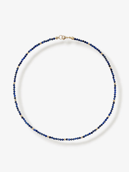 Dainty lapis lazuli gemstone beaded necklace with blue faceted round beads and gold accent beads and clasp with minimalist design on a neutral background