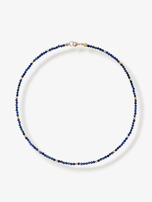 Dainty lapis lazuli gemstone beaded necklace with blue faceted round beads and gold accent beads and clasp with minimalist design on a neutral background