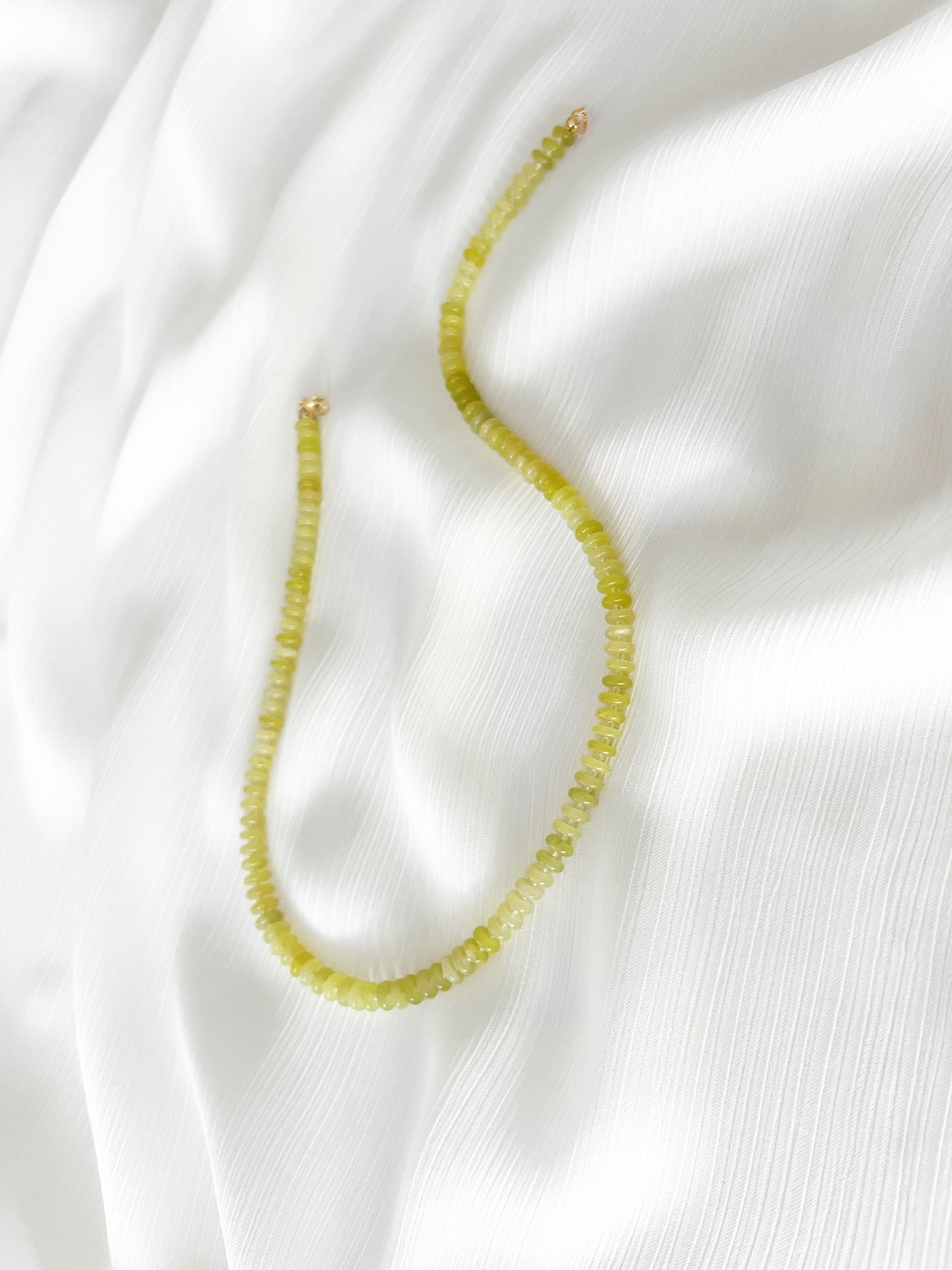 Lemon jade beaded gemstone necklace with smooth disc rondelle beads and sparkling Japanese seed bead accents, finished with 14k gold filled accent beads and clasp on a soft white fabric background