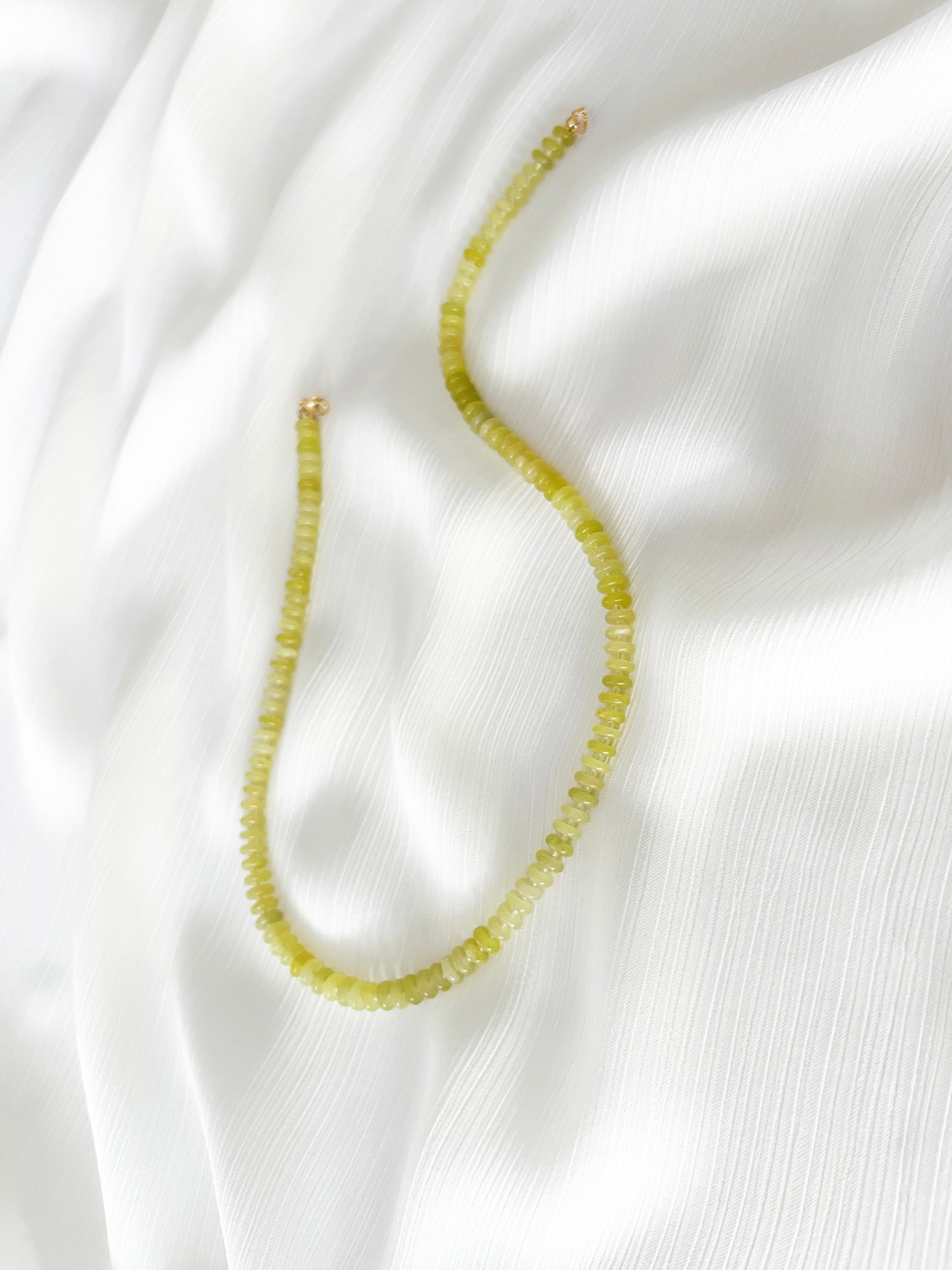 Lemon jade beaded gemstone necklace with smooth disc rondelle beads and sparkling Japanese seed bead accents, finished with 14k gold filled accent beads and clasp on a soft white fabric background