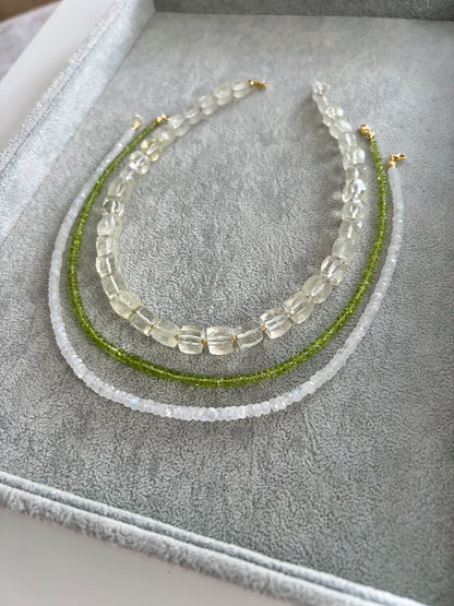 Three gemstone necklaces on a grey velvet tray: chunky lemon quartz cubes with gold filled accent beads, peridot smooth rondelle, and moonstone faceted rondelle, all with 14k solid gold or gold filled clasps