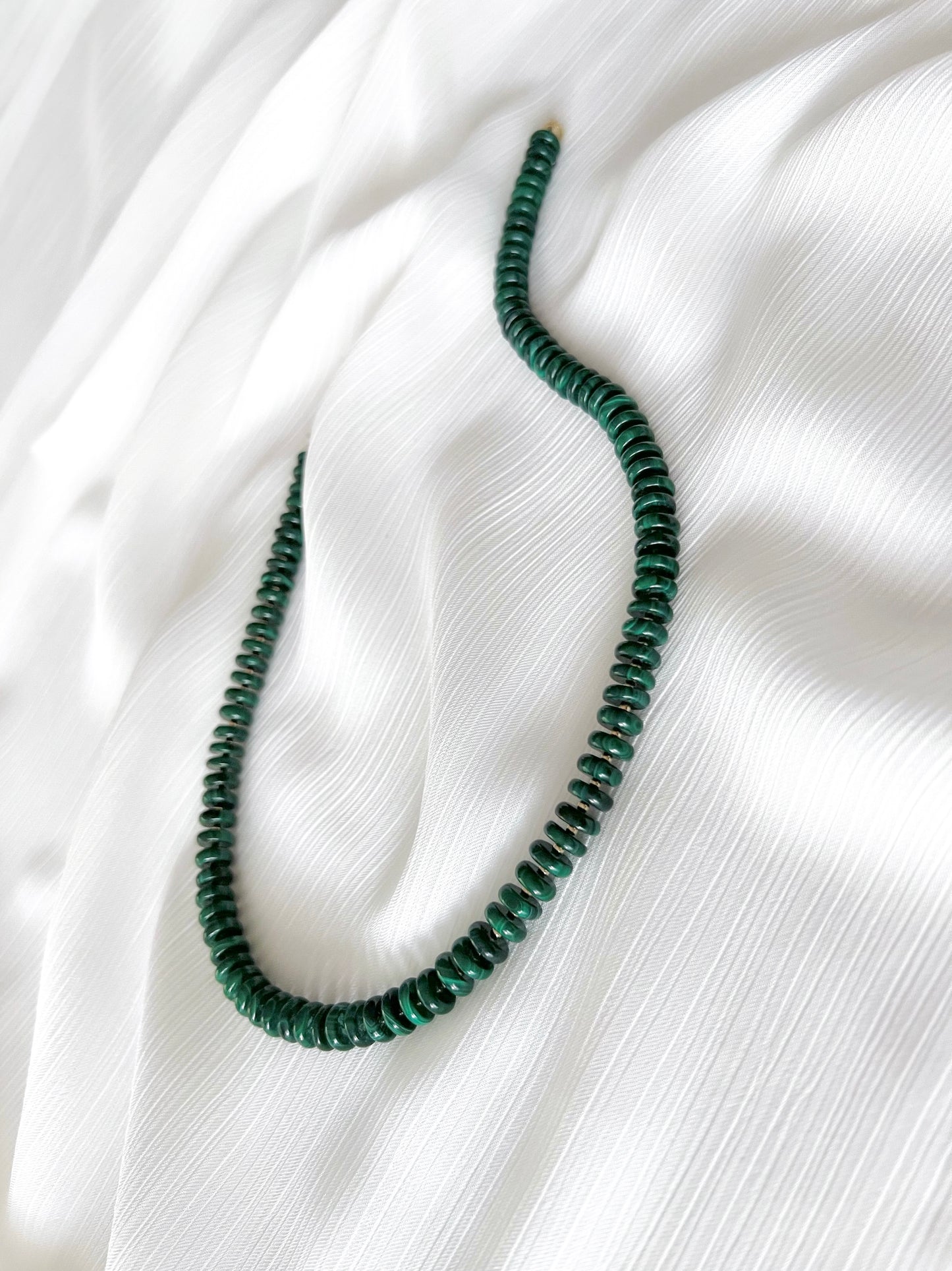 Chunky malachite beaded gemstone necklace with dark green smooth disc rondelle beads finished with 14k gold filled accent beads and clasp on a soft white fabric background