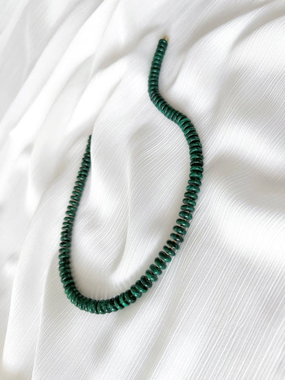 Chunky malachite beaded gemstone necklace with dark green smooth disc rondelle beads finished with 14k gold filled accent beads and clasp on a soft white fabric background