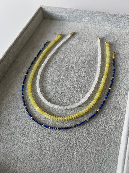 Three gemstone beaded necklaces on a grey velvet tray: rainbow moonstone faceted rondelle, lemon jade smooth disc rondelle, and lapis lazuli faceted round with 14k solid gold or gold filled accents and gold filled clasps