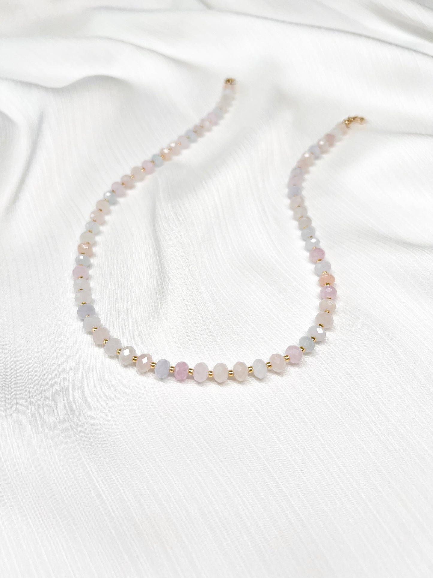 Dainty morganite beaded gemstone necklace with soft pastel hues of blush pink, peach, blues and green, with faceted rondelle beads finished with 14k gold filled accent beads and clasp on a soft white fabric background