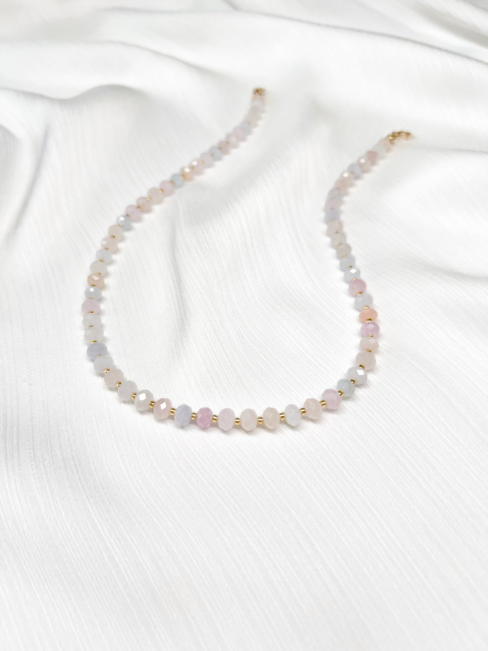 Dainty morganite beaded gemstone necklace with soft pastel hues of blush pink, peach, blues and green, with faceted rondelle beads finished with 14k gold filled accent beads and clasp on a soft white fabric background