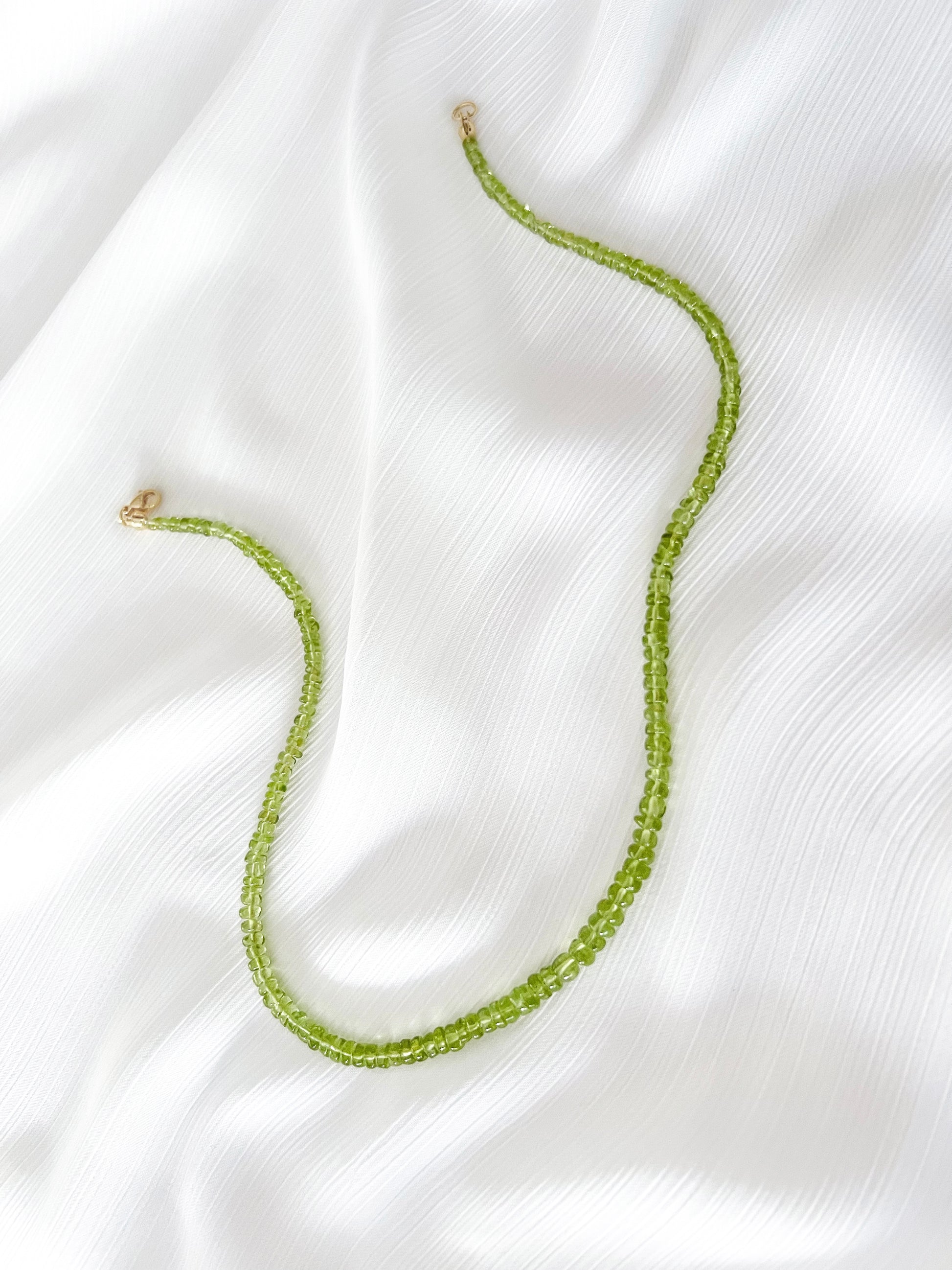 Peridot beaded gemstone necklace with green smooth rondelle beads and 14k solid gold or gold filled clasp with minimalist design on soft white fabric