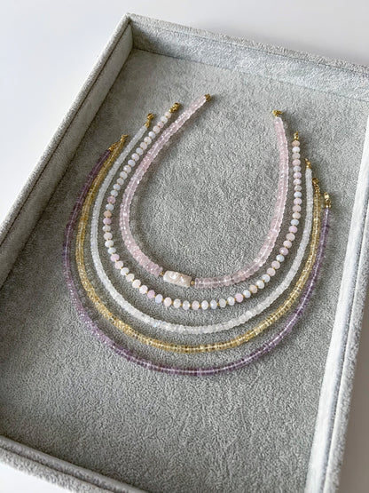 Four gemstone necklaces on a grey velvet tray: chunky faceted rose quartz with a freshwater keshi pearl centerpiece, morganite with faceted rondelle beads and gold filled accents, rainbow moonstone faceted rondelle, citrine smooth rondelle, and pink amethyst smooth rondelle