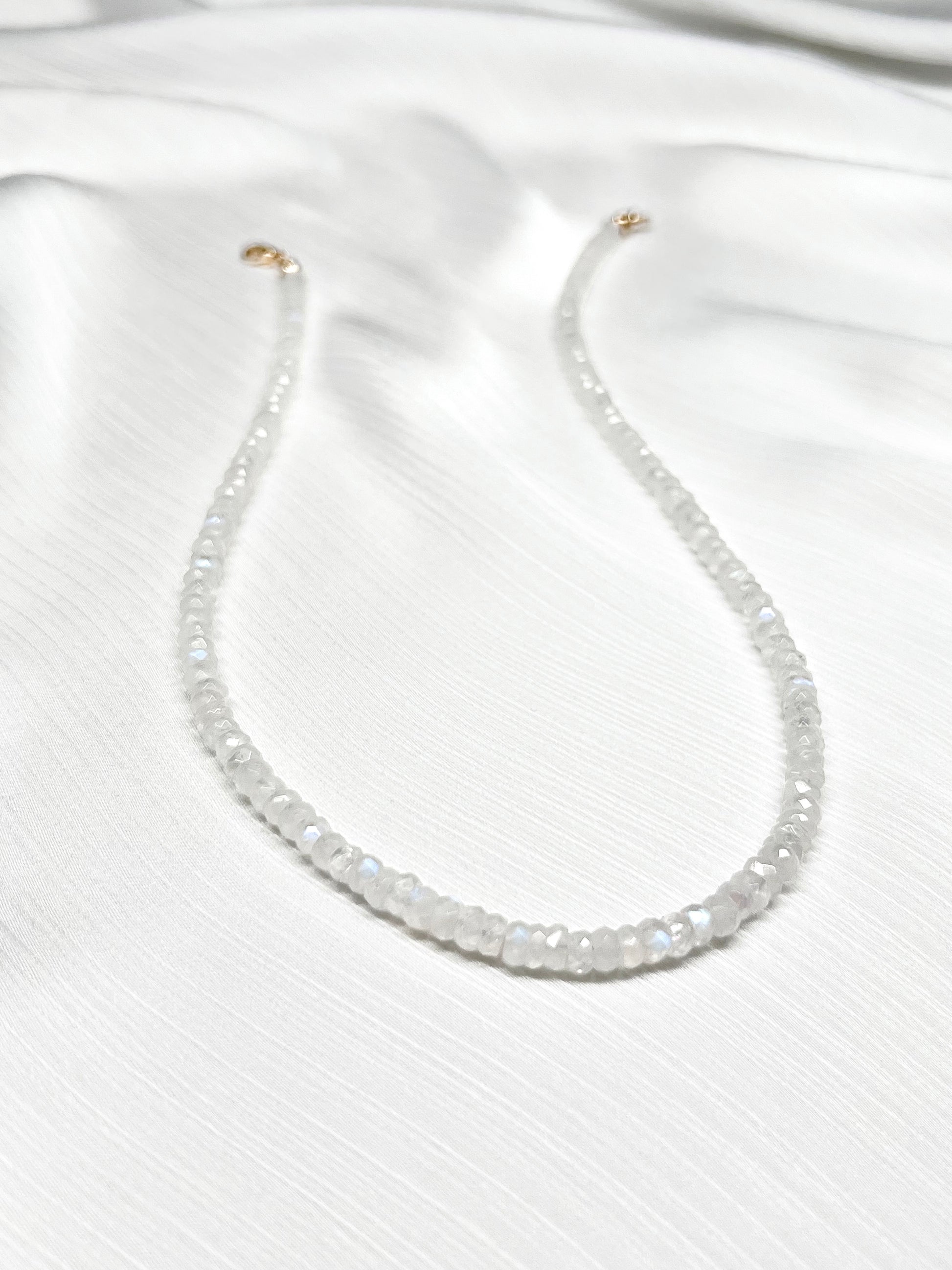 Rainbow moonstone beaded gemstone necklace with white faceted rondelle beads and 14k solid gold or gold filled clasp with minimalist design on a soft white fabric background