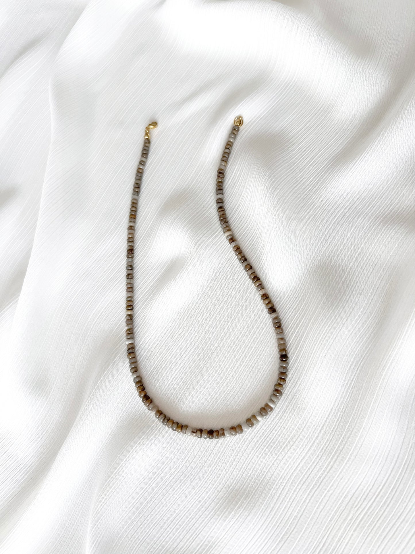 Dainty silver leaf jasper beaded gemstone necklace with rondelle beads featuring a multi-tone or neutral shades including beige, tan, brown, grey, and white with smooth polished finish completed with 14k gold filled or solid gold clasp with a minimalist design on a soft white fabric background