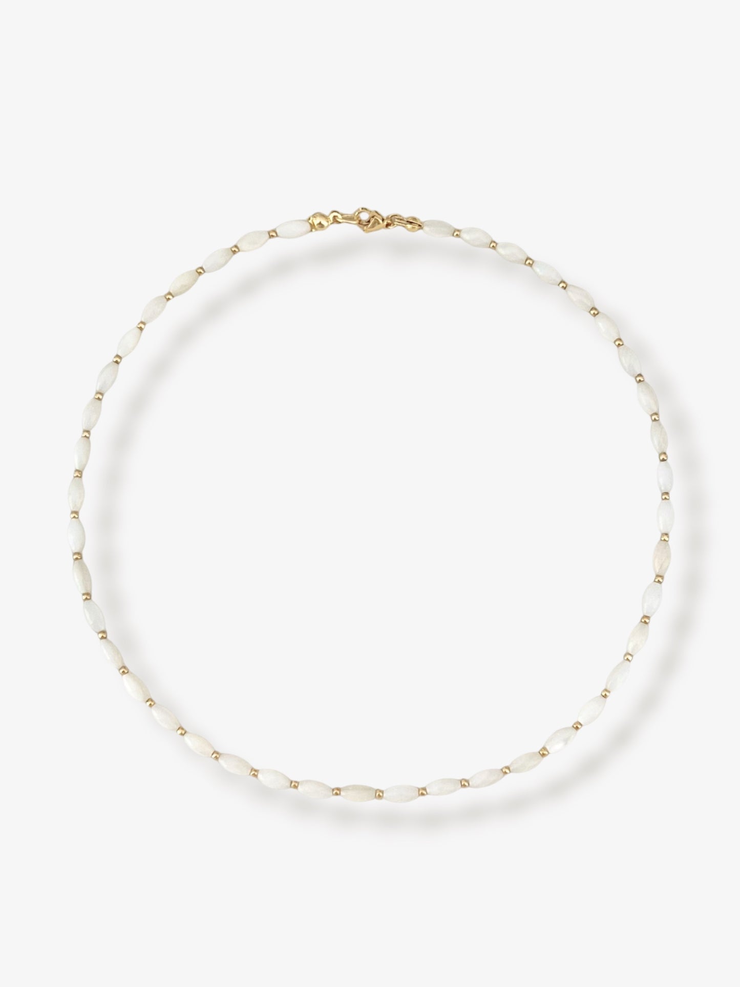 Dainty natural shell beaded necklace with white rice shaped shell beads and 14k gold filled accent beads and clasp. Minimalist layering necklace on a neutral background