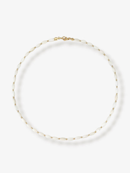 Dainty natural shell beaded necklace with white rice shaped shell beads and 14k gold filled accent beads and clasp. Minimalist layering necklace on a neutral background