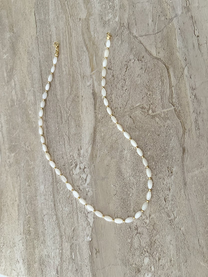 Dainty natural shell beaded necklace with white rice shaped shell beads and 14k gold filled accent beads and clasp. Minimalist layering necklace on a luxury stone slab background